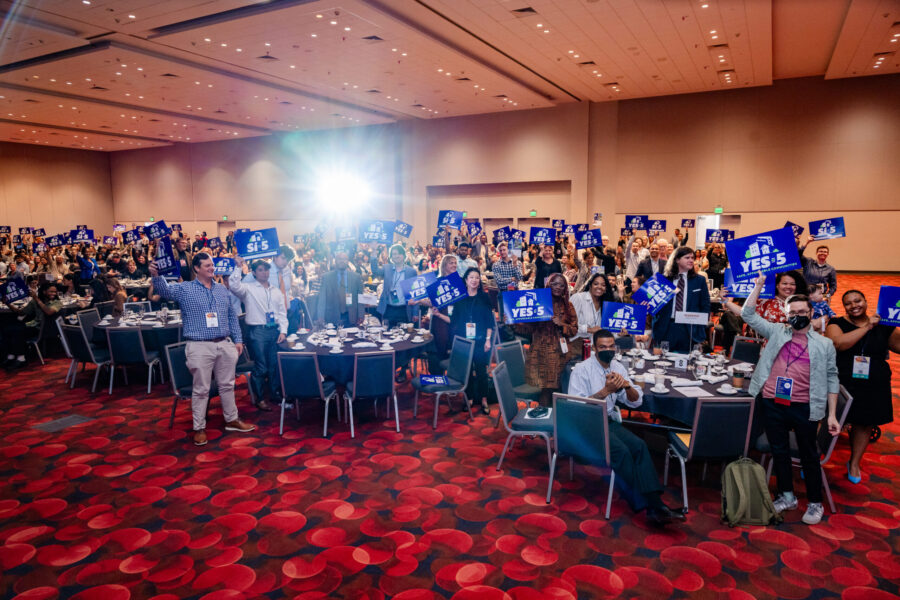 People inside a large meeting room holding signs